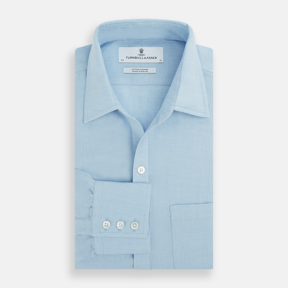 The Blue Cotton Cashmere Chelsea Shirt by Turnbull & Asser, a light blue long-sleeve button-up with a chest pocket, crafted from soft cotton and cashmere, is shown laid flat on a white background.