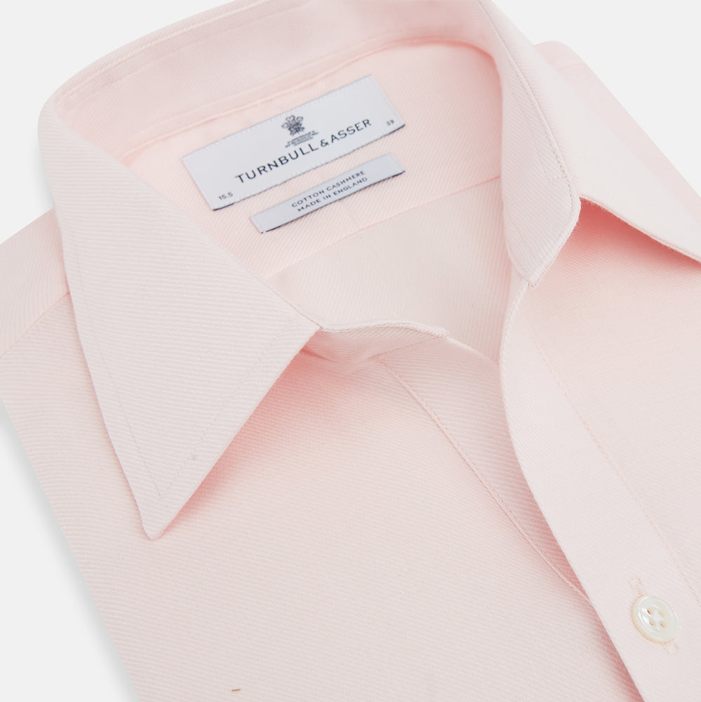 The Turnbull & Asser Pale Pink Cotton Cashmere Chelsea Shirt features long sleeves, a chest pocket, spread collar, and buttoned cuffs. Crafted from a luxurious cotton-cashmere blend, it's shown laid flat on a white background.
