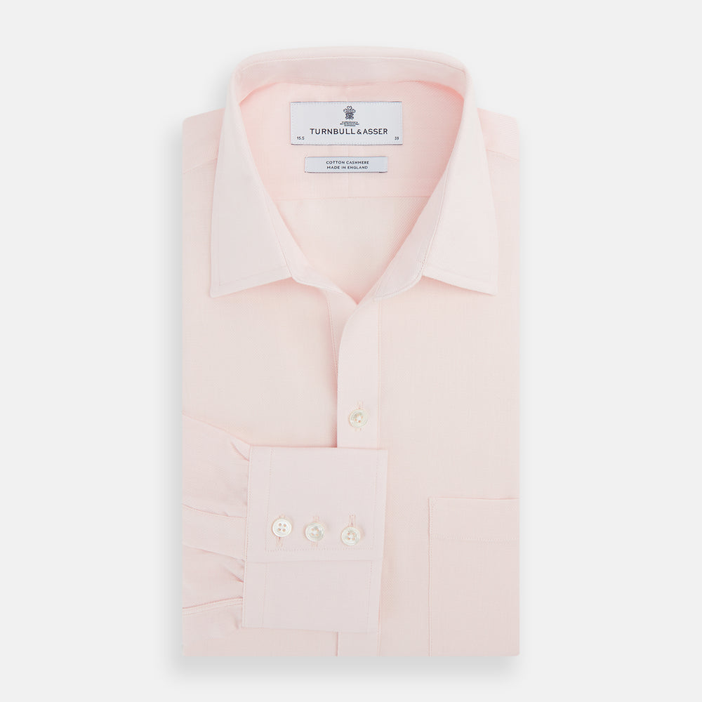 The Turnbull & Asser Pale Pink Cotton Cashmere Chelsea Shirt features long sleeves, a chest pocket, spread collar, and buttoned cuffs. Crafted from a luxurious cotton-cashmere blend, it's shown laid flat on a white background.