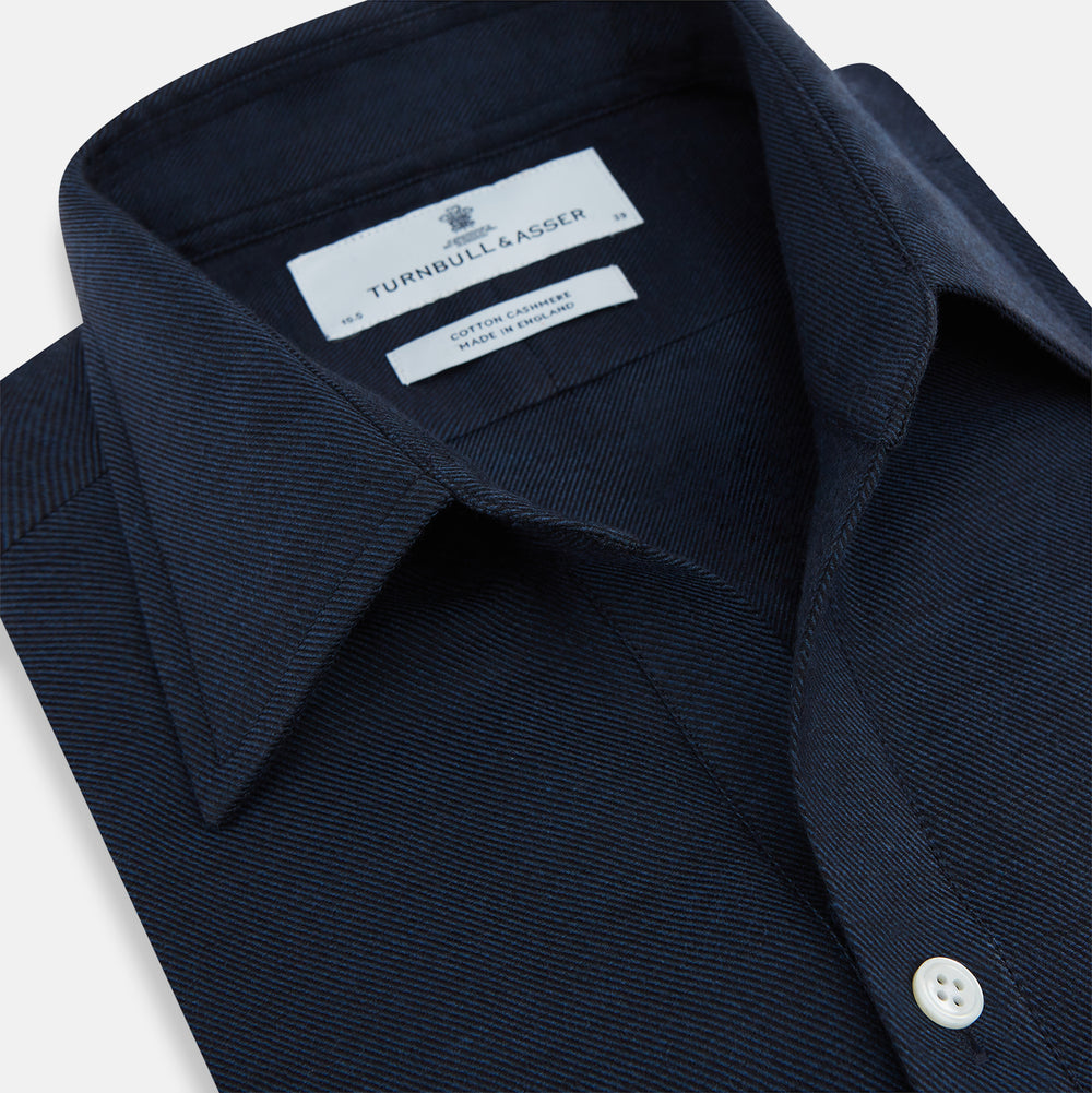 The Turnbull & Asser Navy Cotton Cashmere Chelsea Shirt features long sleeves, a classic collar, front chest pocket, and white buttons, shown laid flat on a white background.