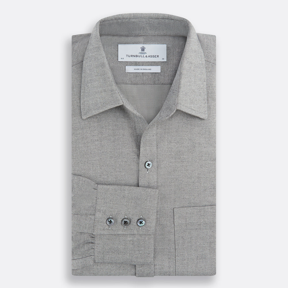 The Turnbull & Asser Grey Herringbone Chelsea Shirt features long sleeves, a chest pocket, classic collar, and buttoned cuffs, adding refined style to smart-casual outfits—shown here against a plain white background.