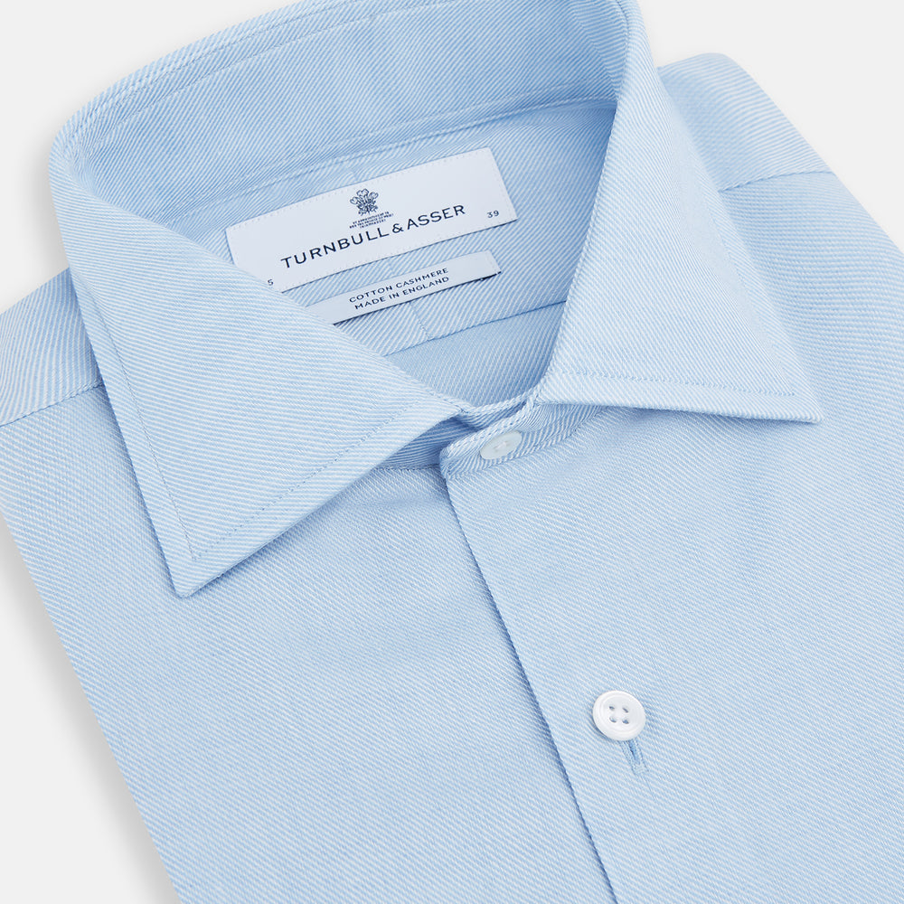 The Turnbull & Asser Tailored Fit Blue Cotton Cashmere Belgravia Shirt features a classic collar, button-down front, and buttoned cuffs, shown laid flat on a white background for a refined, formal look.