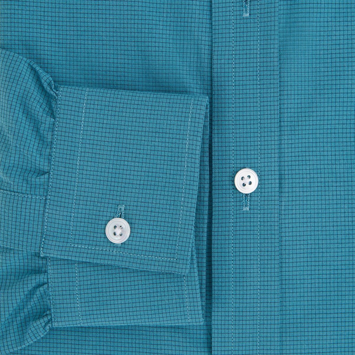 View 4 of product Here’s a rewritten version using your product data: The Turnbull & Asser UK Fine Checked Turquoise Blue Weekend Fit Shirt in Cotton is a men’s long-sleeve button-up, featuring a chest pocket, white buttons, and a pointed collar, shown laid flat against a white background.