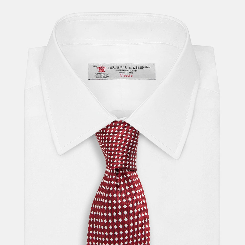 The Turnbull & Asser Slim Burgundy and White Diamond Silk Tie, shown rolled on a white background, features a repeating pattern of small white diamonds—an ideal accessory to complement any office shirt.
