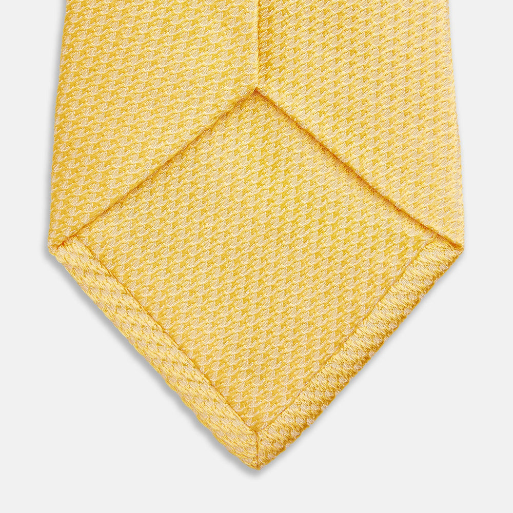 The Turnbull & Asser Yellow Lace Silk Tie, featuring a light yellow hue and subtle texture, is neatly rolled and displayed on a plain white background.