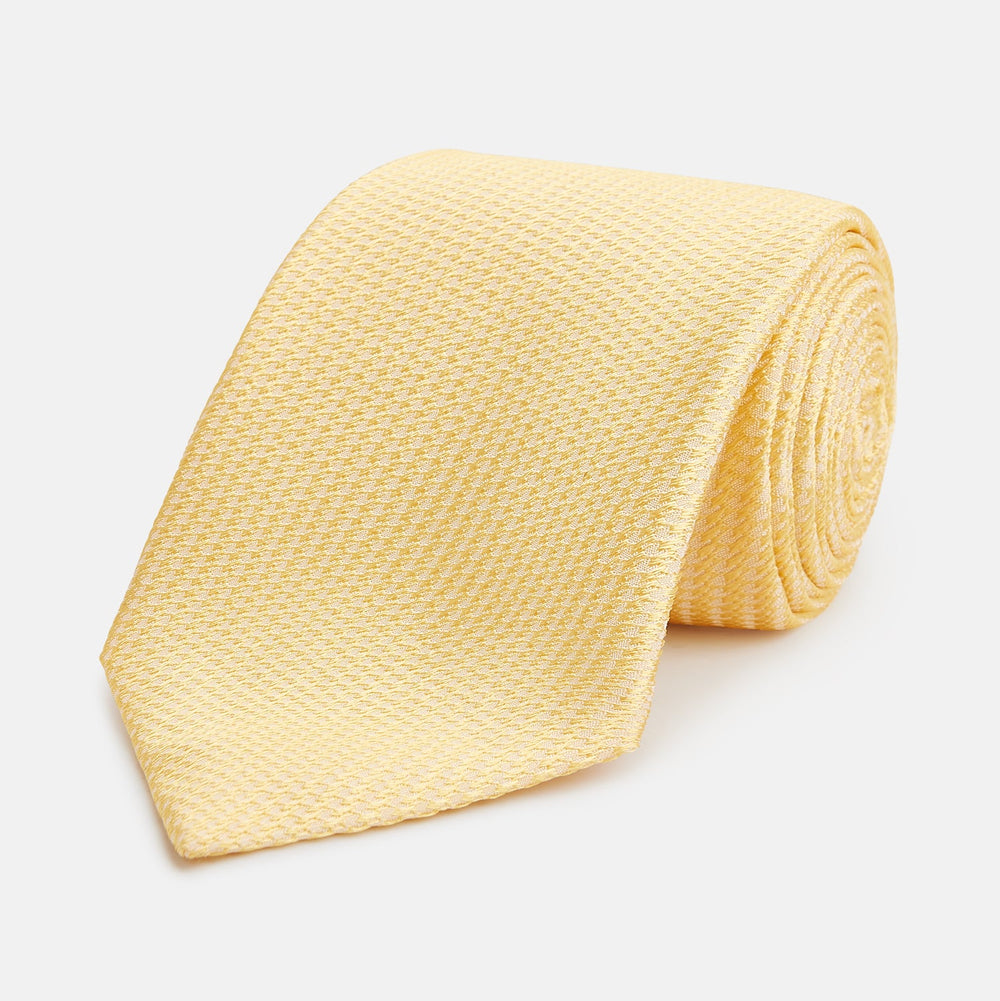 The Turnbull & Asser Yellow Lace Silk Tie, featuring a light yellow hue and subtle texture, is neatly rolled and displayed on a plain white background.