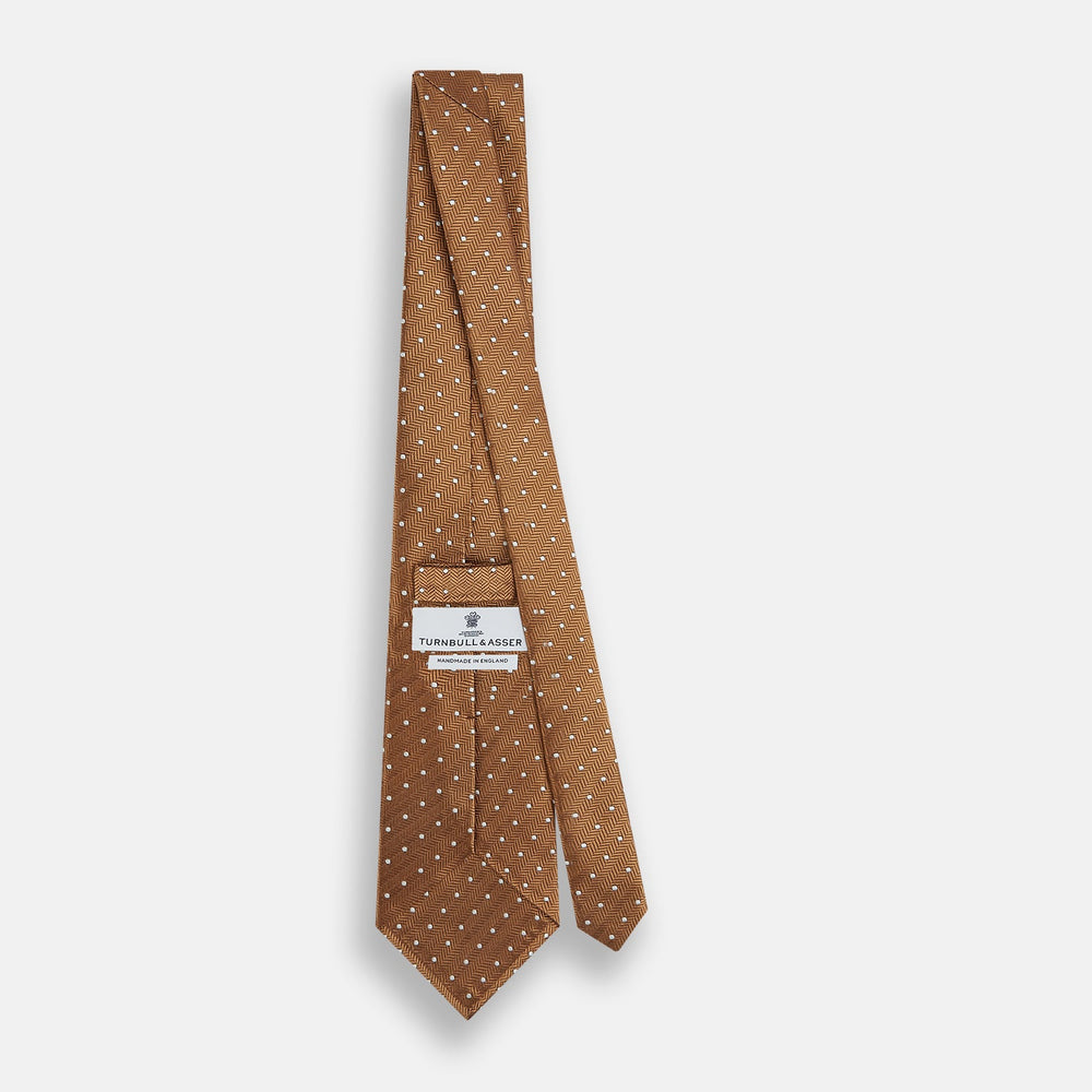 The Turnbull & Asser Camel and White Small Spot Herringbone Silk Tie features a stylish herringbone pattern with white spots—an elegant accessory ideal for modern office attire.