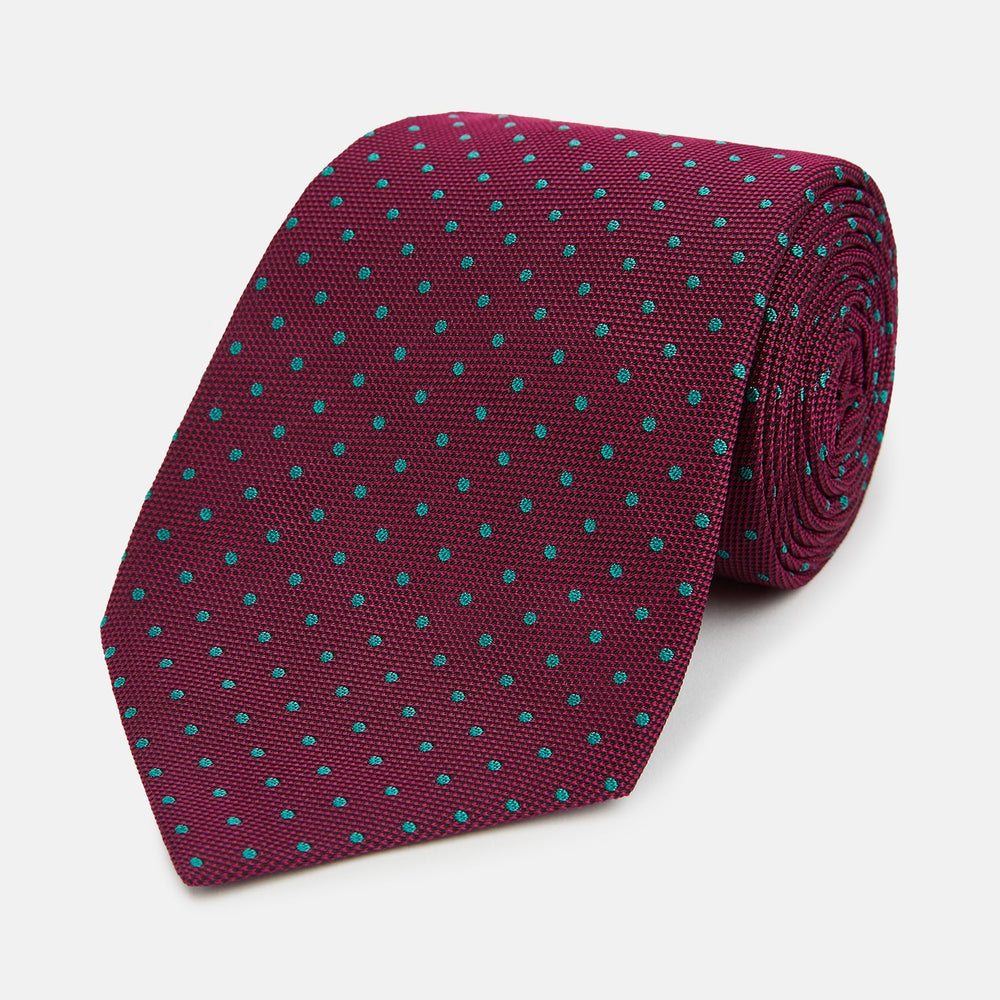 A rolled-up Turnbull & Asser Green and Magenta Micro Dot Silk Tie, featuring small, evenly spaced magenta dots on green silk, displayed on a plain white background—an ideal accessory for sophisticated outfits.