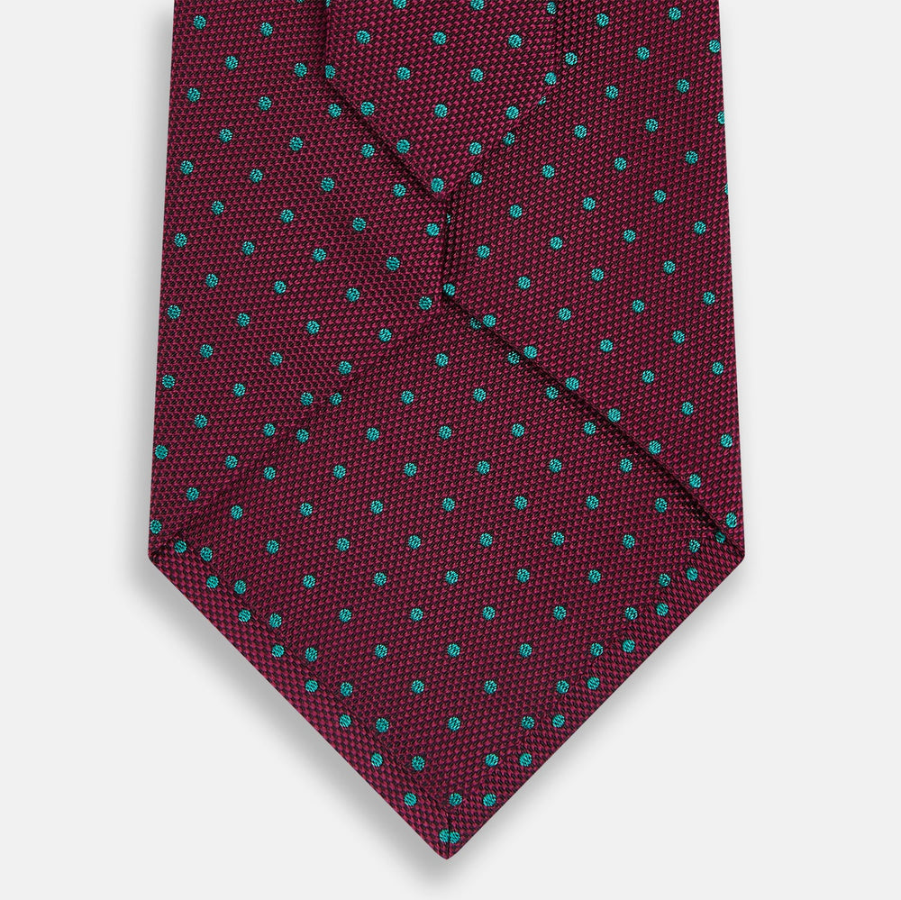 A rolled-up Turnbull & Asser Green and Magenta Micro Dot Silk Tie, featuring small, evenly spaced magenta dots on green silk, displayed on a plain white background—an ideal accessory for sophisticated outfits.