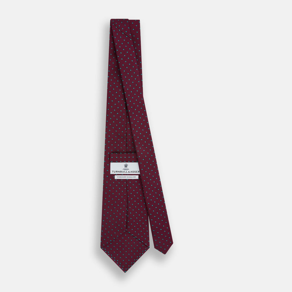 A rolled-up Turnbull & Asser Green and Magenta Micro Dot Silk Tie, featuring small, evenly spaced magenta dots on green silk, displayed on a plain white background—an ideal accessory for sophisticated outfits.