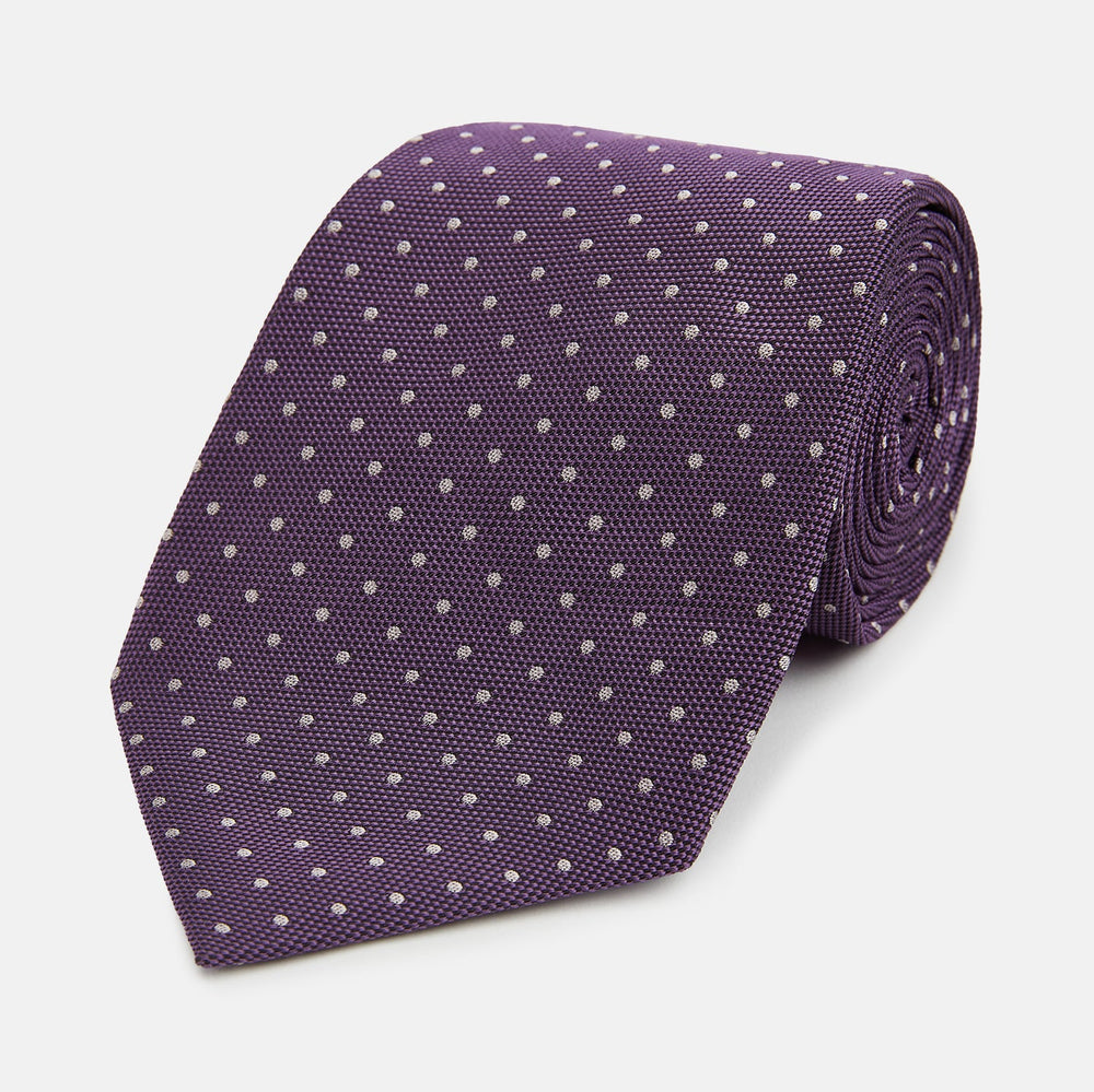 The Turnbull & Asser Lilac and Purple Micro Dot Silk Tie, featuring a subtle white micro-dot pattern, is rolled up and displayed on a white background—an essential addition to any polished wardrobe.