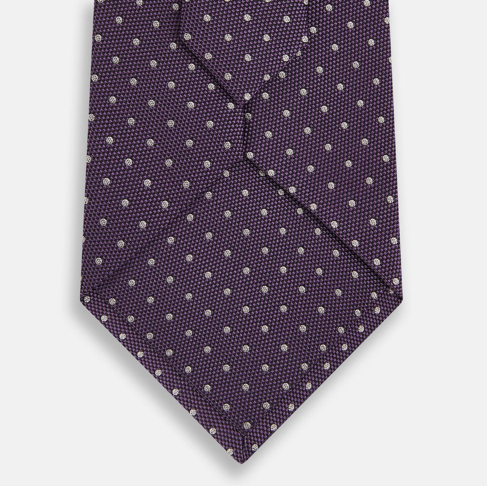 The Turnbull & Asser Lilac and Purple Micro Dot Silk Tie, featuring a subtle white micro-dot pattern, is rolled up and displayed on a white background—an essential addition to any polished wardrobe.