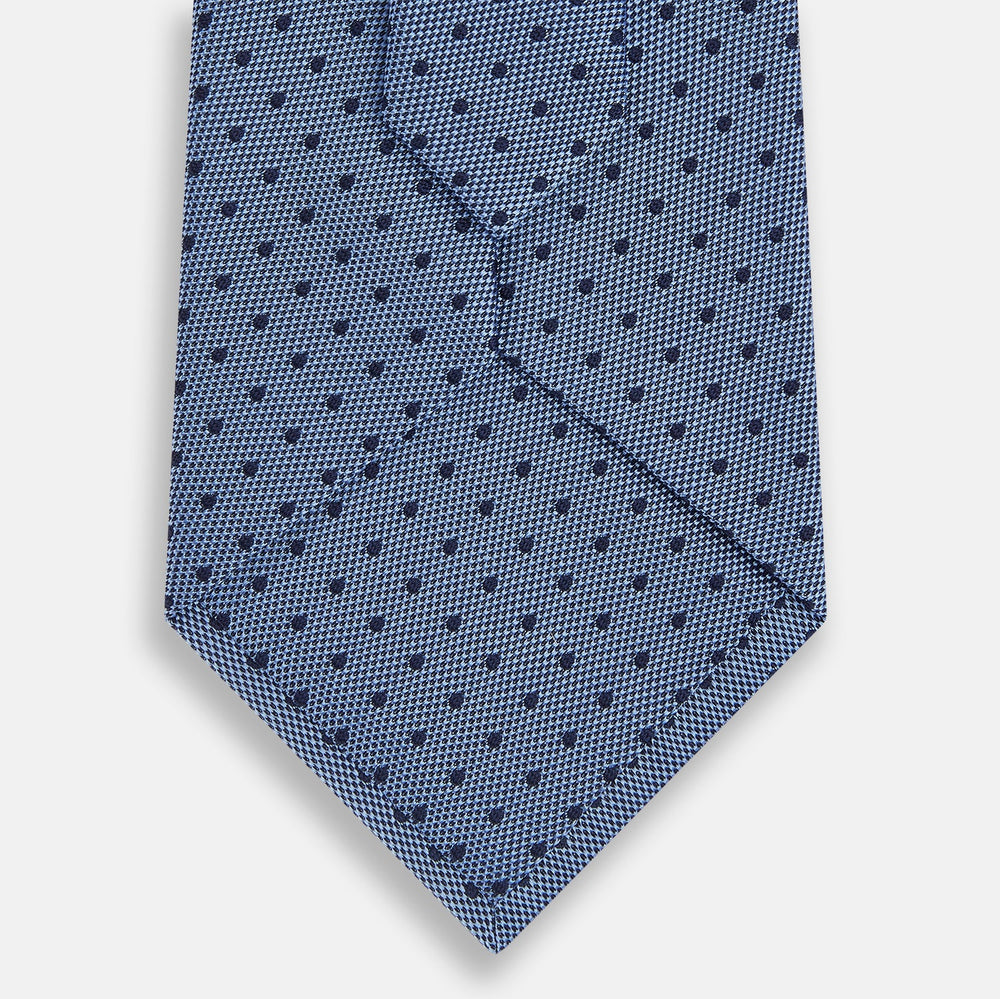 The Turnbull & Asser Navy and Blue Micro Dot Silk Tie is shown rolled up, featuring a steel blue color with small navy blue dots, on a plain white background.