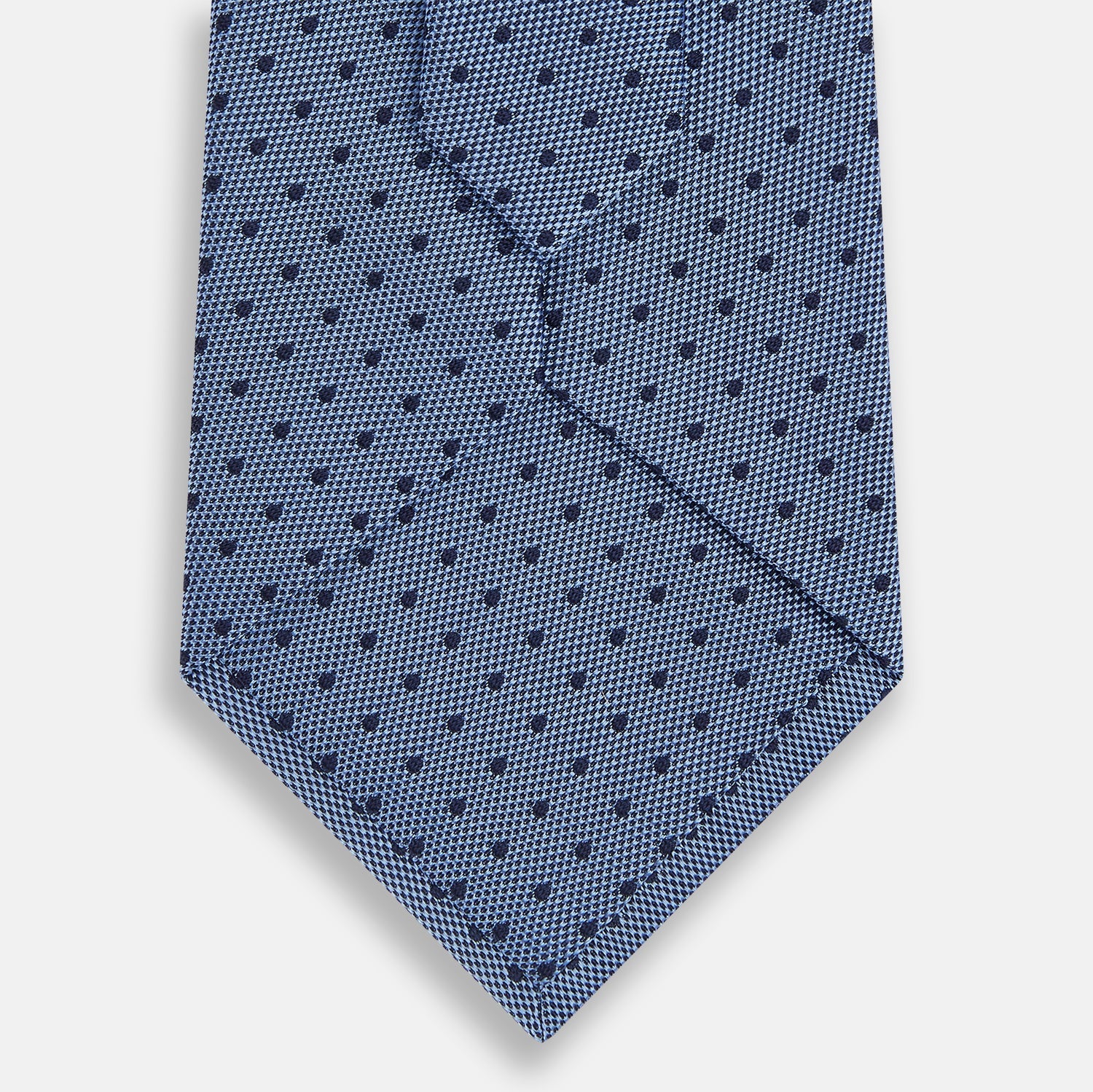 View 3 of product The Turnbull & Asser Navy and Blue Micro Dot Silk Tie is shown rolled up, featuring a steel blue color with small navy blue dots, on a plain white background.