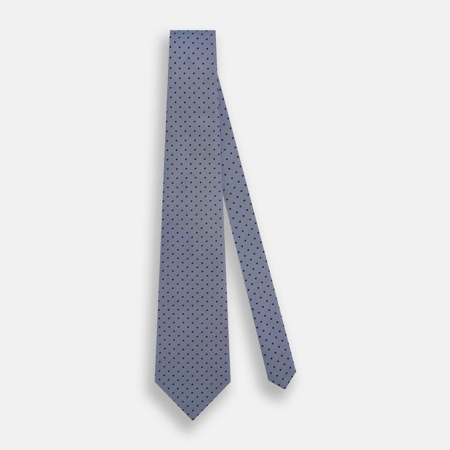 View 2 of product The Turnbull & Asser Navy and Pale Blue Micro Dot Silk Tie features a pattern of small, evenly spaced dots and is elegantly rolled on a plain white background.