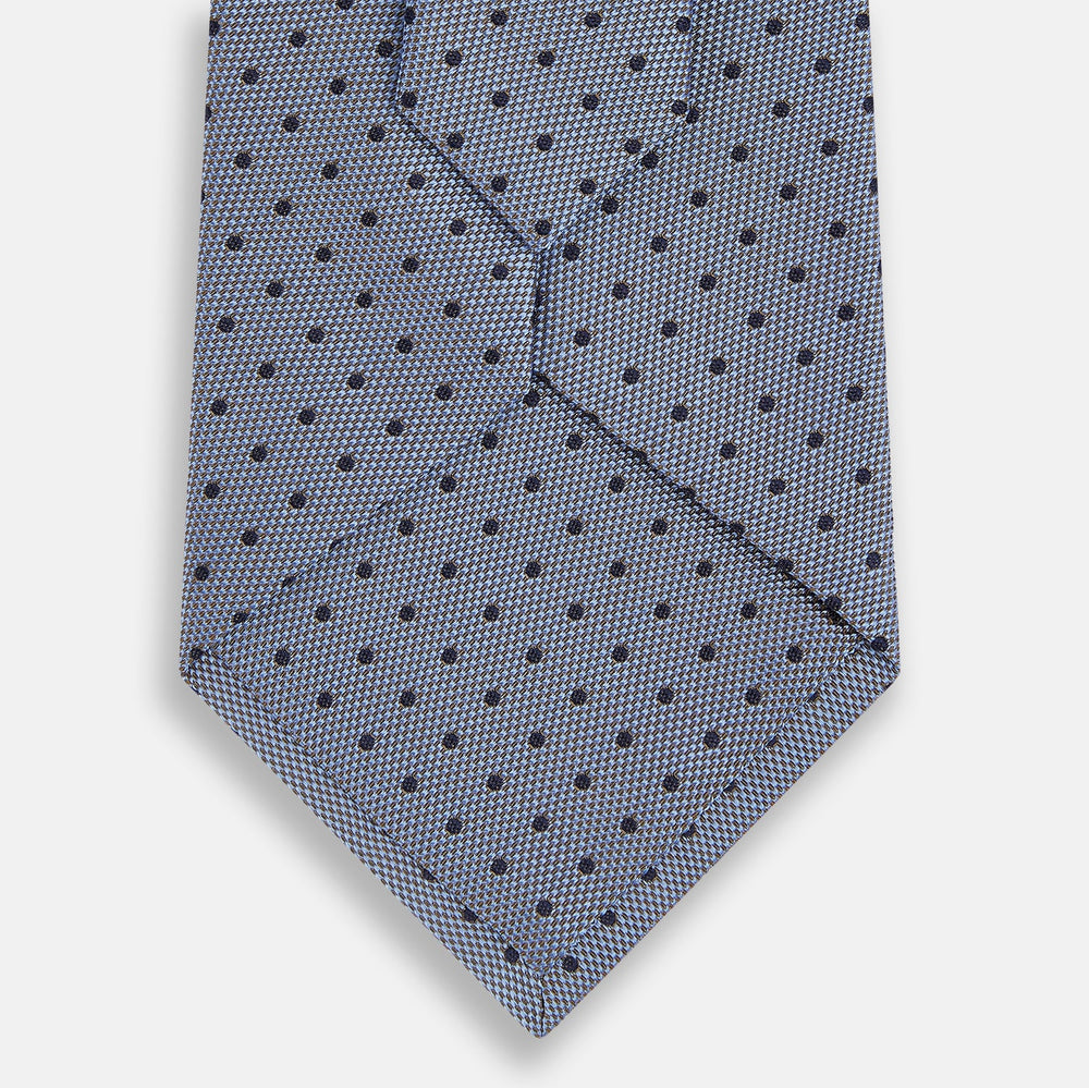 The Turnbull & Asser Navy and Pale Blue Micro Dot Silk Tie features a pattern of small, evenly spaced dots and is elegantly rolled on a plain white background.