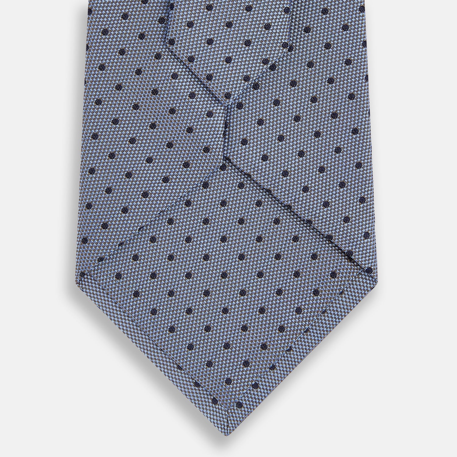 View 3 of product The Turnbull & Asser Navy and Pale Blue Micro Dot Silk Tie features a pattern of small, evenly spaced dots and is elegantly rolled on a plain white background.