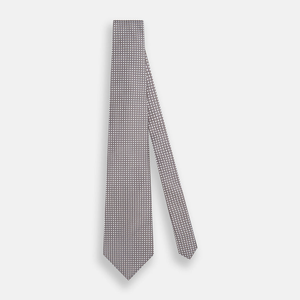 The Turnbull & Asser Grey and White Diamond Silk Tie features a refined geometric pattern, combining silver triangles on a white background for an elegant look.