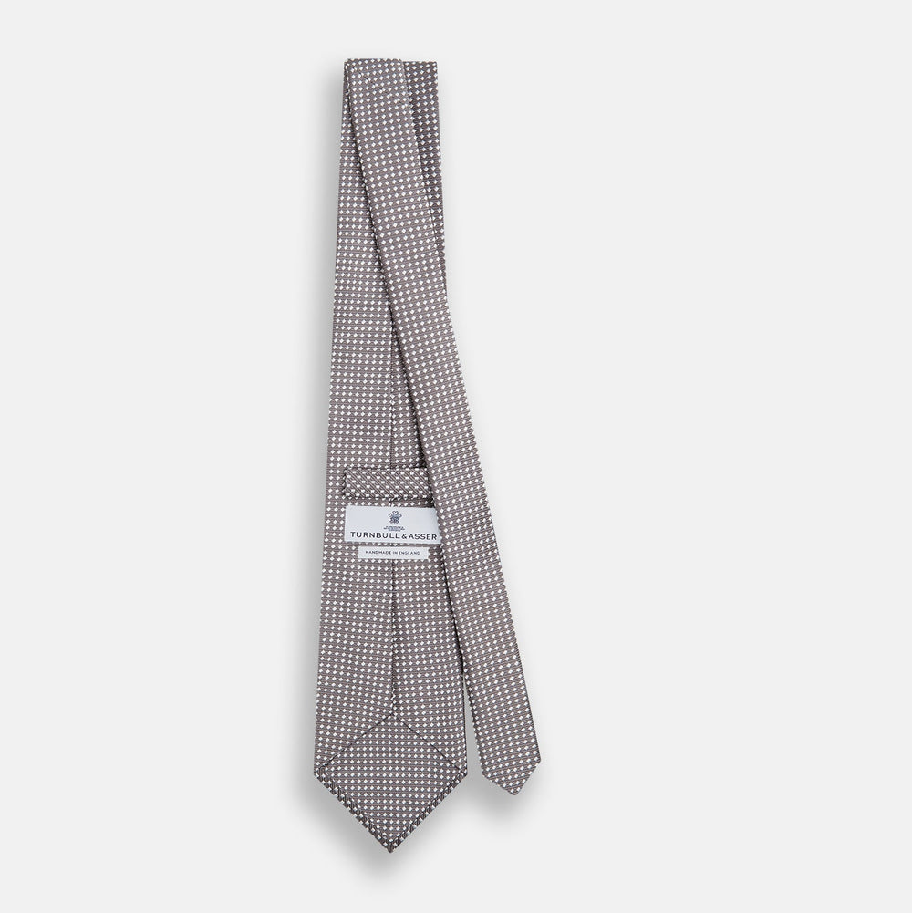 The Turnbull & Asser Grey and White Diamond Silk Tie features a refined geometric pattern, combining silver triangles on a white background for an elegant look.