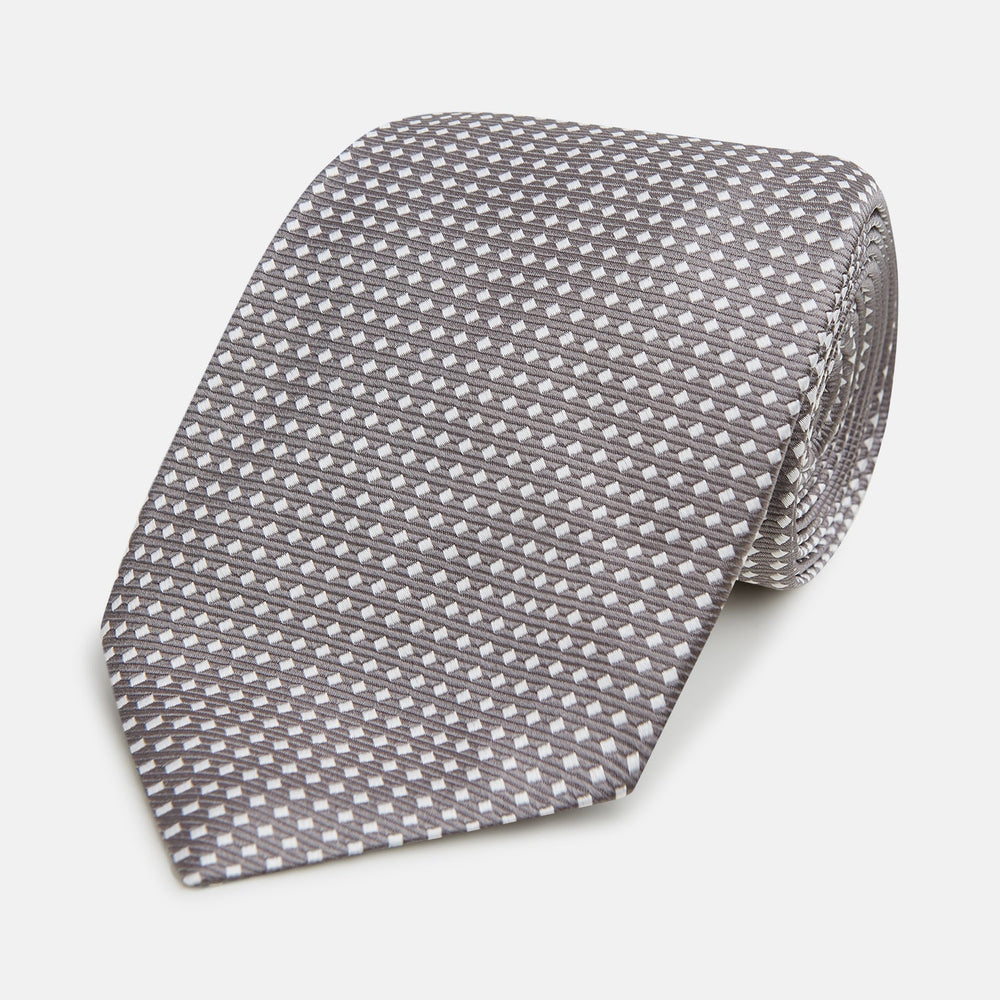 The Turnbull & Asser Grey and White Diamond Silk Tie features a refined geometric pattern, combining silver triangles on a white background for an elegant look.