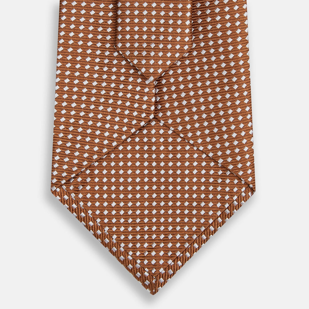 The Turnbull & Asser Brown and White Diamond Silk Tie features a repeating small geometric pattern and is displayed rolled up on a plain white background.