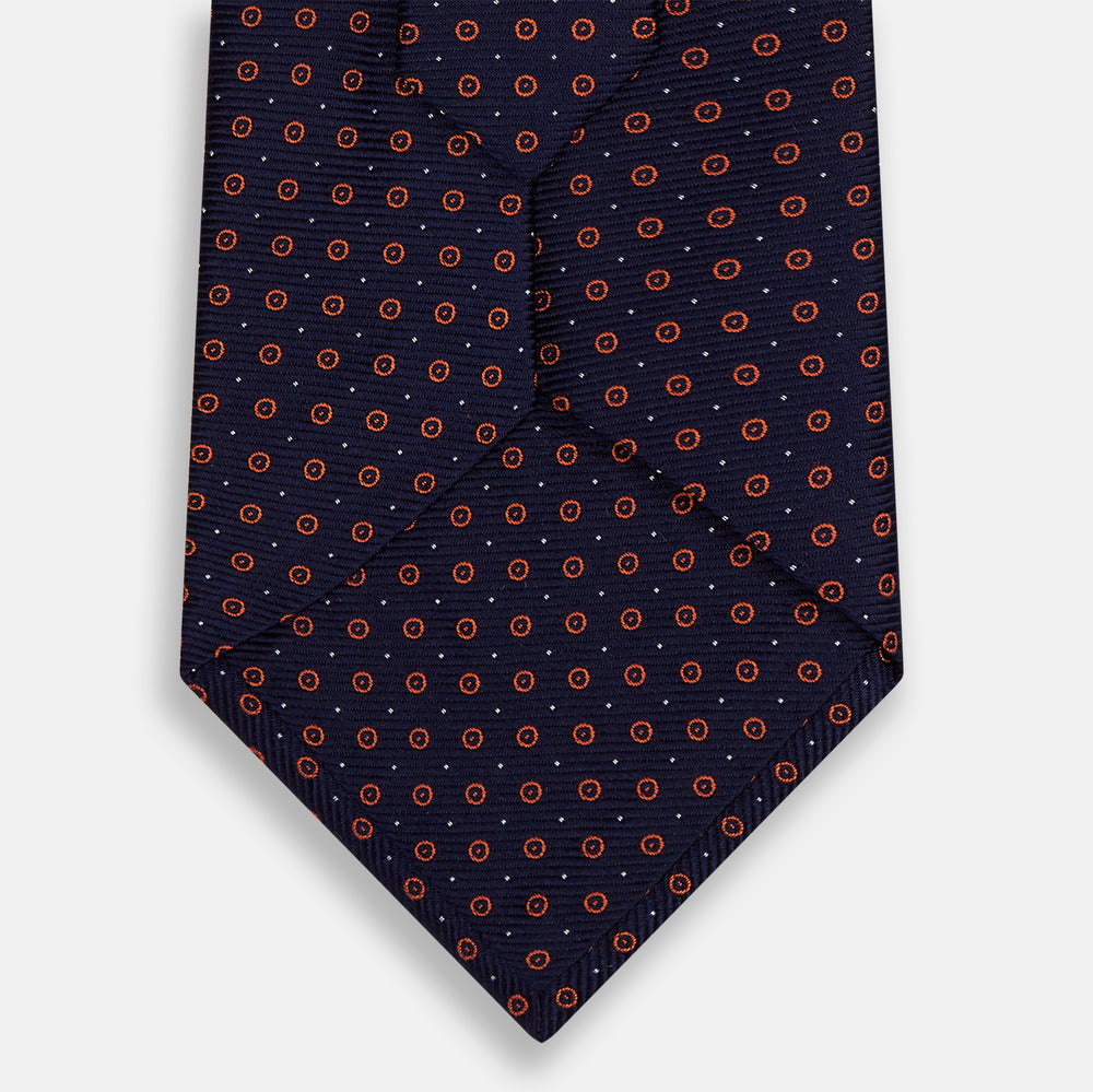 A Navy and Orange Circle Silk Tie by Turnbull & Asser, neatly rolled on a white background.