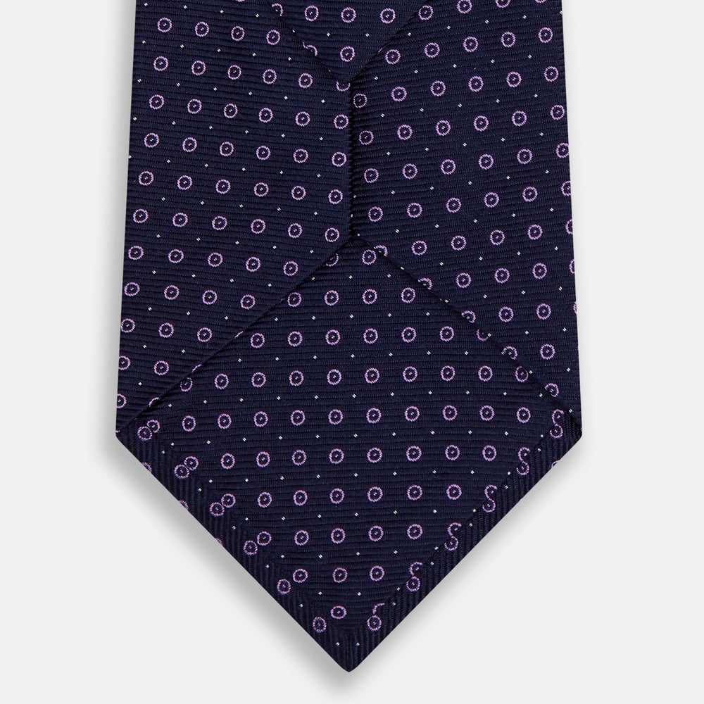 The Navy and Lilac Circle Silk Tie by Turnbull & Asser features pink and purple circles on dark navy silk, shown rolled on a white background—ideal for formal occasions.