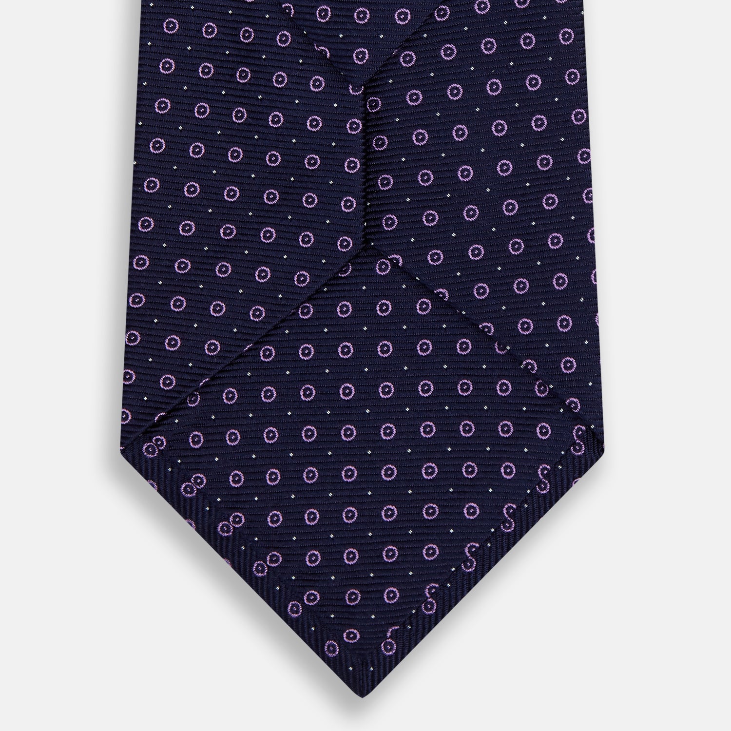 View 3 of product The Navy and Lilac Circle Silk Tie by Turnbull & Asser features pink and purple circles on dark navy silk, shown rolled on a white background—ideal for formal occasions.