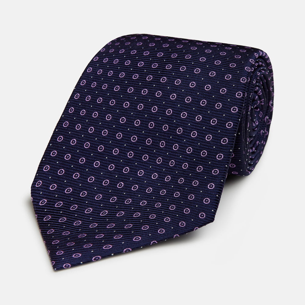 The Navy and Lilac Circle Silk Tie by Turnbull & Asser features pink and purple circles on dark navy silk, shown rolled on a white background—ideal for formal occasions.