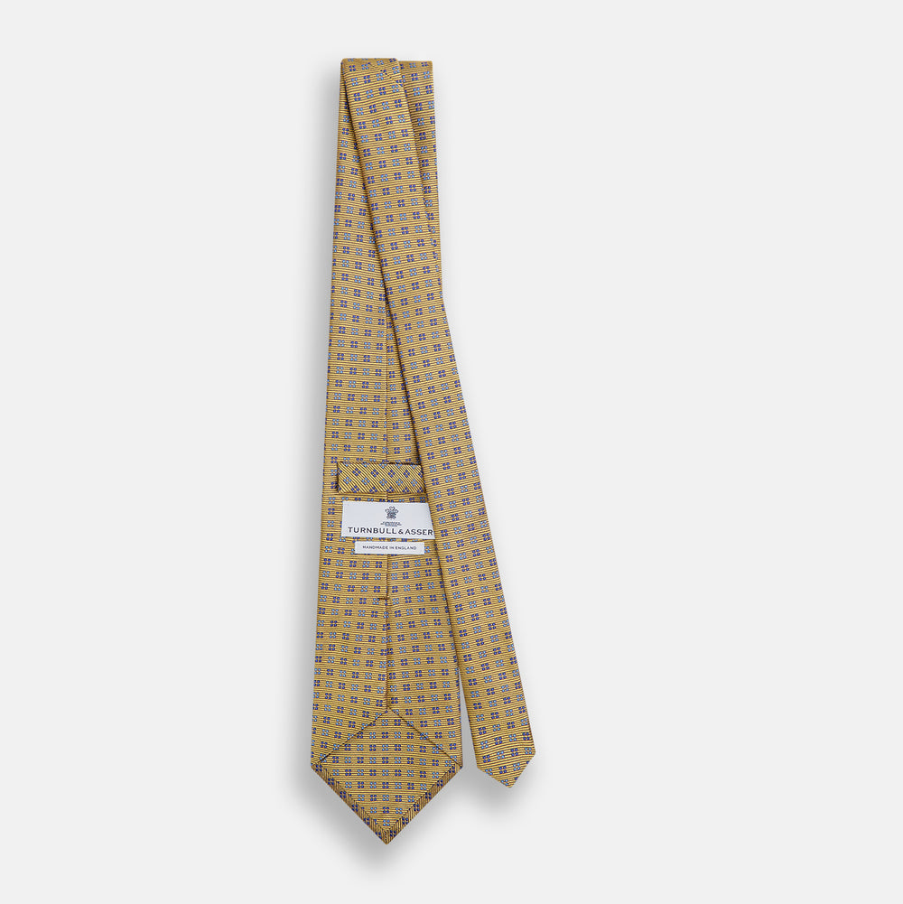 The Turnbull & Asser Blue and Gold Multi Dot Silk Tie features blue and gold dots in neat rows, presented rolled up on a white background.