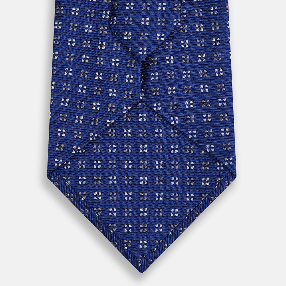 The Turnbull & Asser Blue and Brown Multi Dot Silk Tie, shown rolled up on a plain white background, features an elegant design with small white and gray dots arranged in squares.