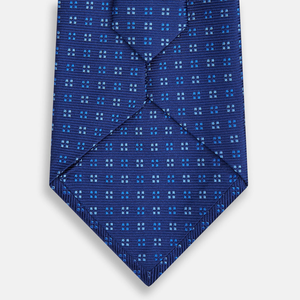 The Turnbull & Asser Blue Multi Dot Silk Tie features a rolled-up blue design with small light blue dots, offering an elegant, refined accent to office attire.