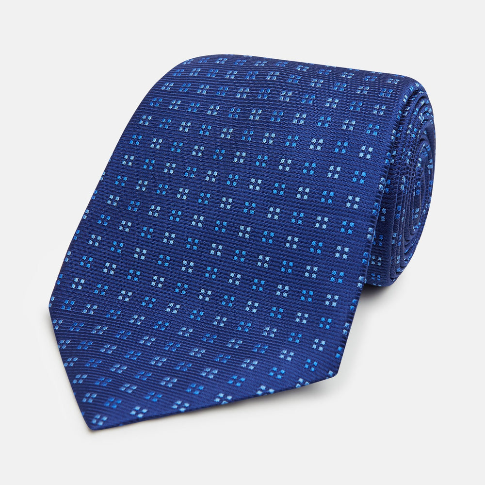 The Turnbull & Asser Blue Multi Dot Silk Tie features a rolled-up blue design with small light blue dots, offering an elegant, refined accent to office attire.