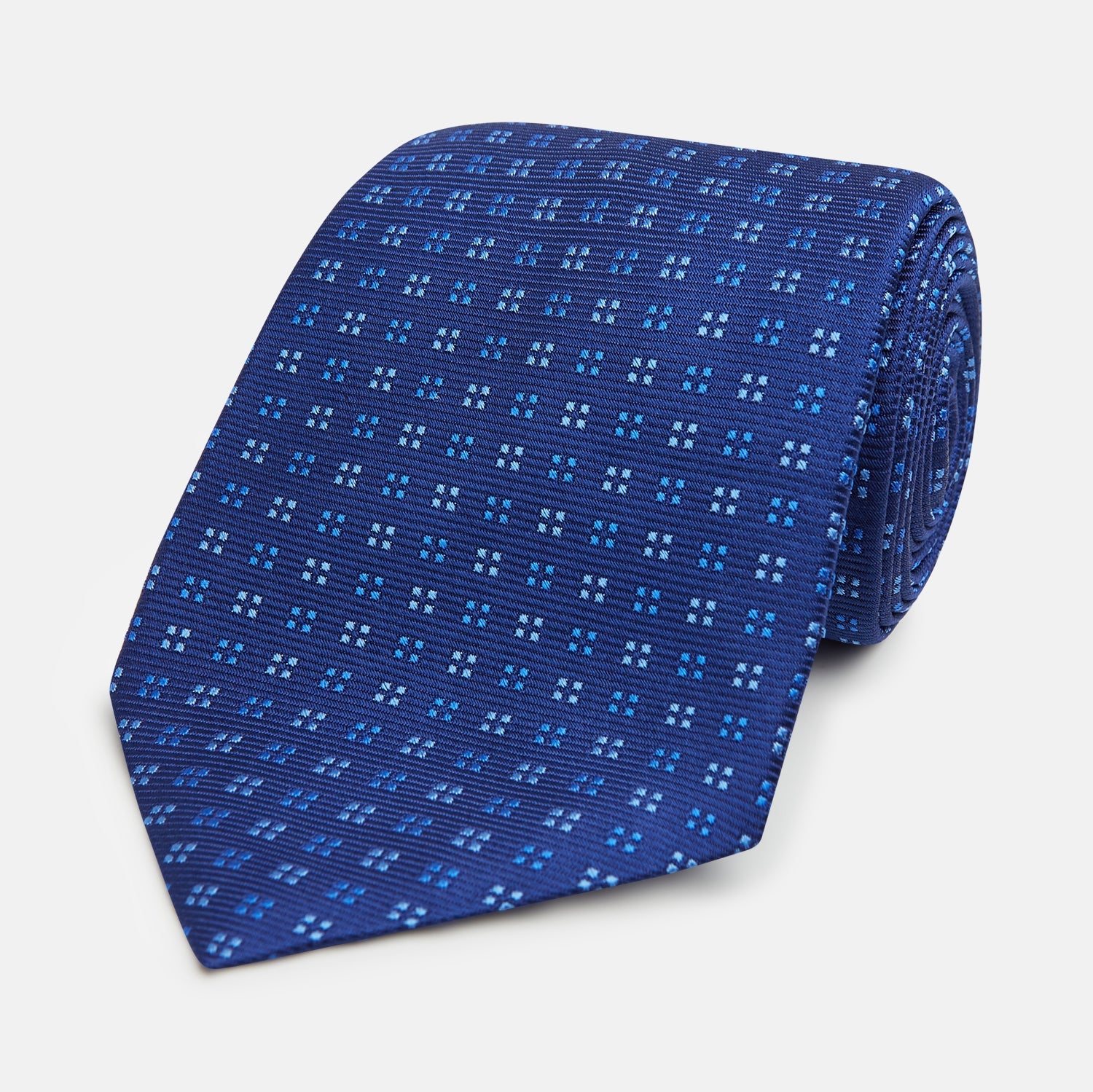 View 1 of product The Turnbull & Asser Blue Multi Dot Silk Tie features a rolled-up blue design with small light blue dots, offering an elegant, refined accent to office attire.