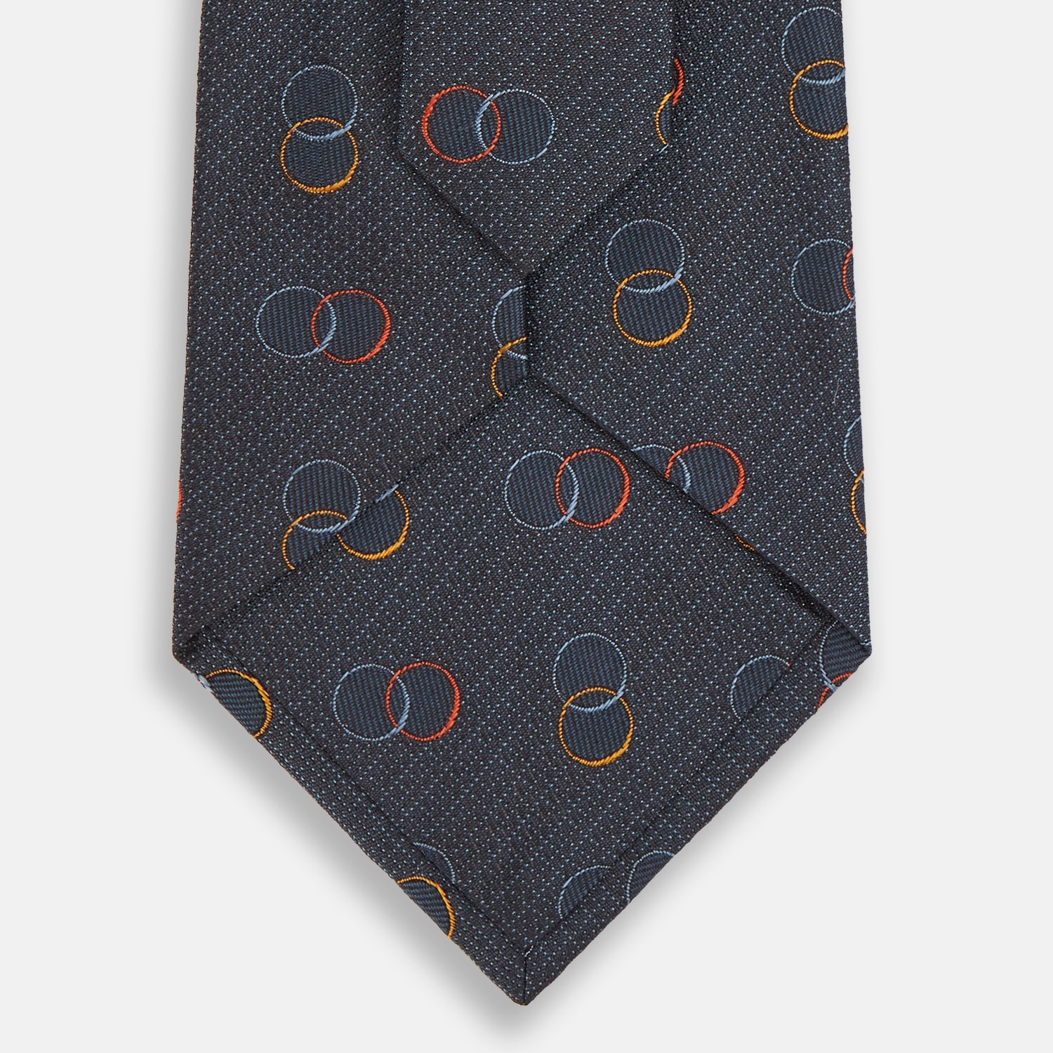 View 3 of product The Navy Links Silk Tie by Turnbull & Asser, featuring a pattern of overlapping red, yellow, and blue rings, is rolled up and displayed against a plain white background.