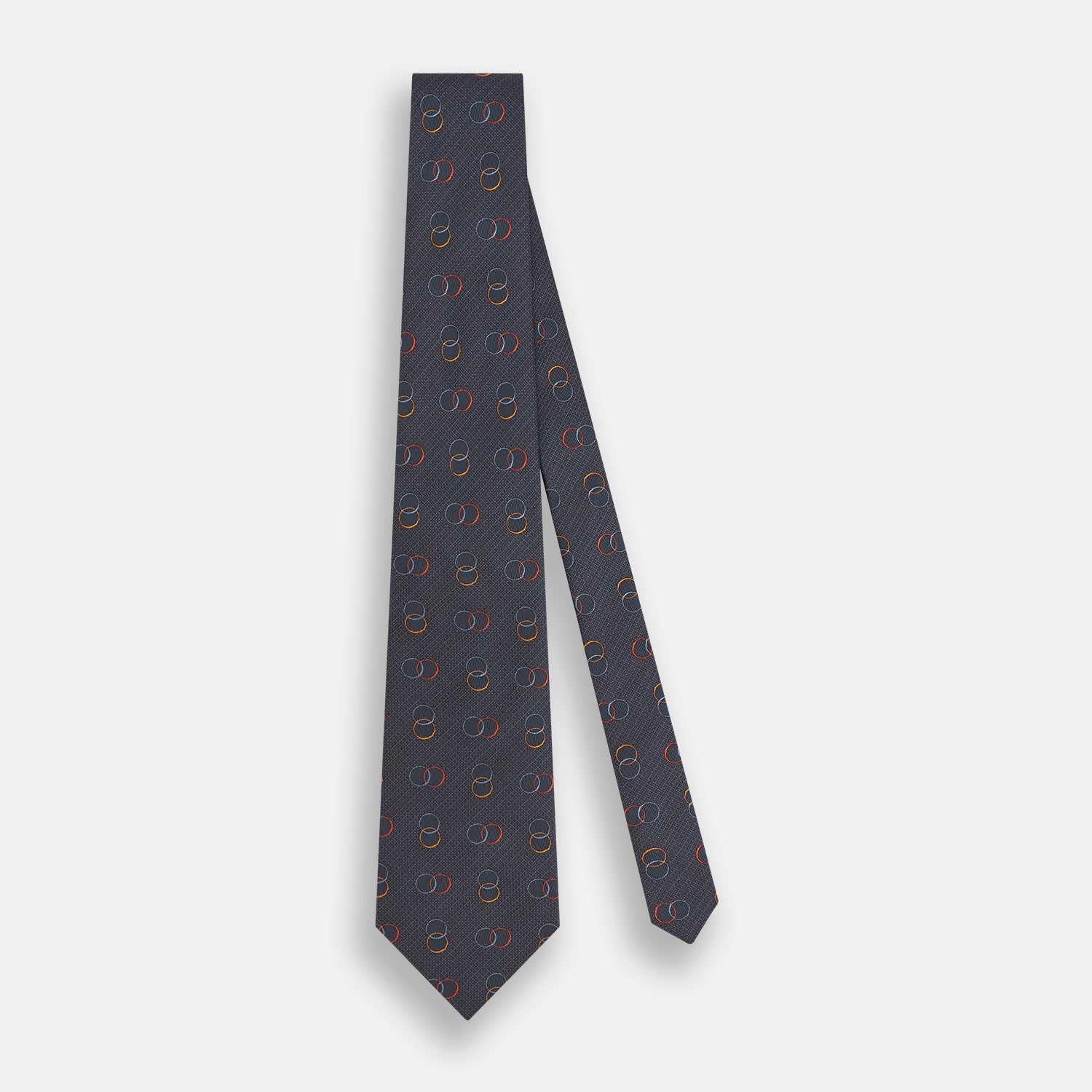 View 2 of product The Navy Links Silk Tie by Turnbull & Asser, featuring a pattern of overlapping red, yellow, and blue rings, is rolled up and displayed against a plain white background.