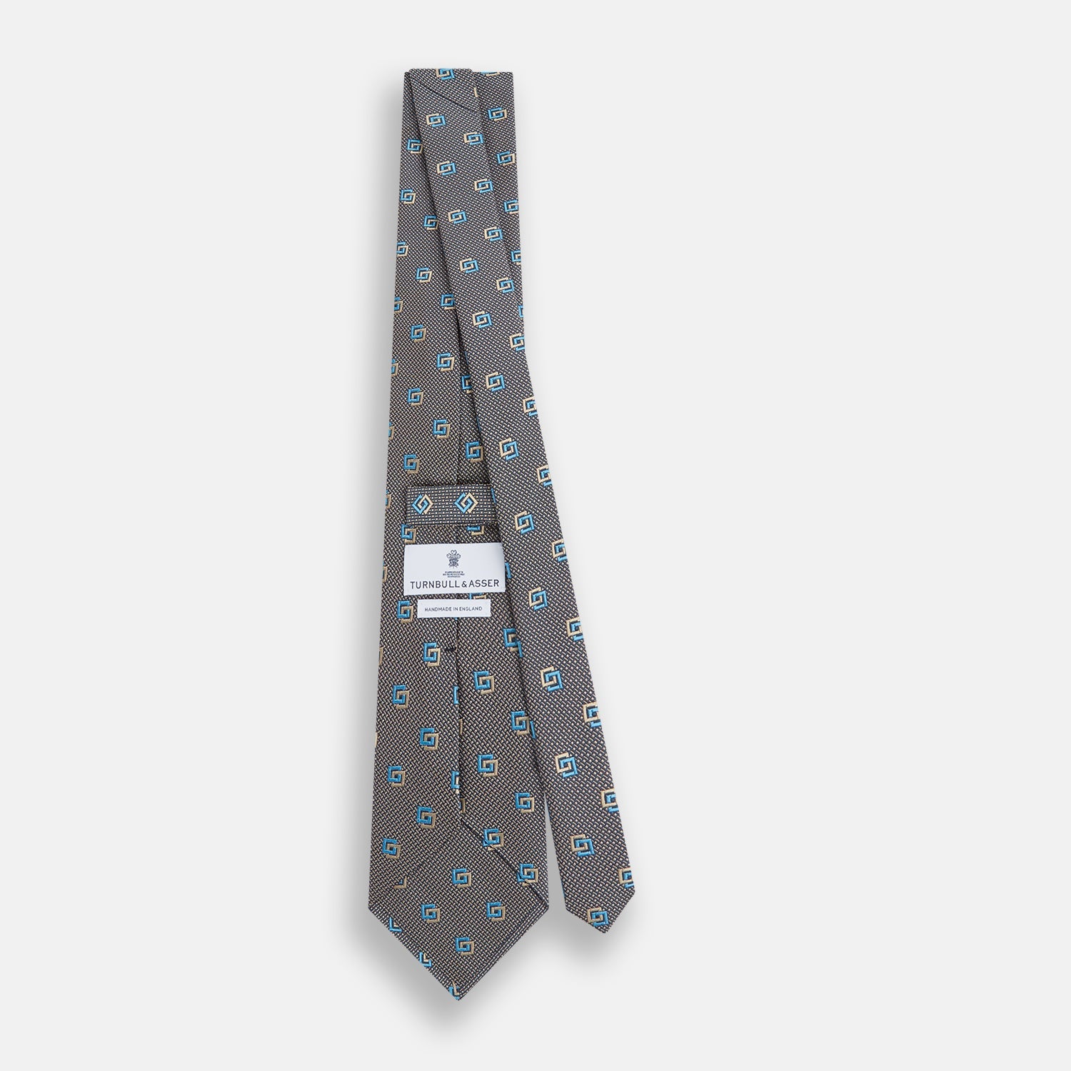 View 4 of product The Turnbull & Asser Blue and Gold Silk Tie, featuring a refined repeating geometric pattern, exudes British elegance and is displayed rolled up on a plain white background.