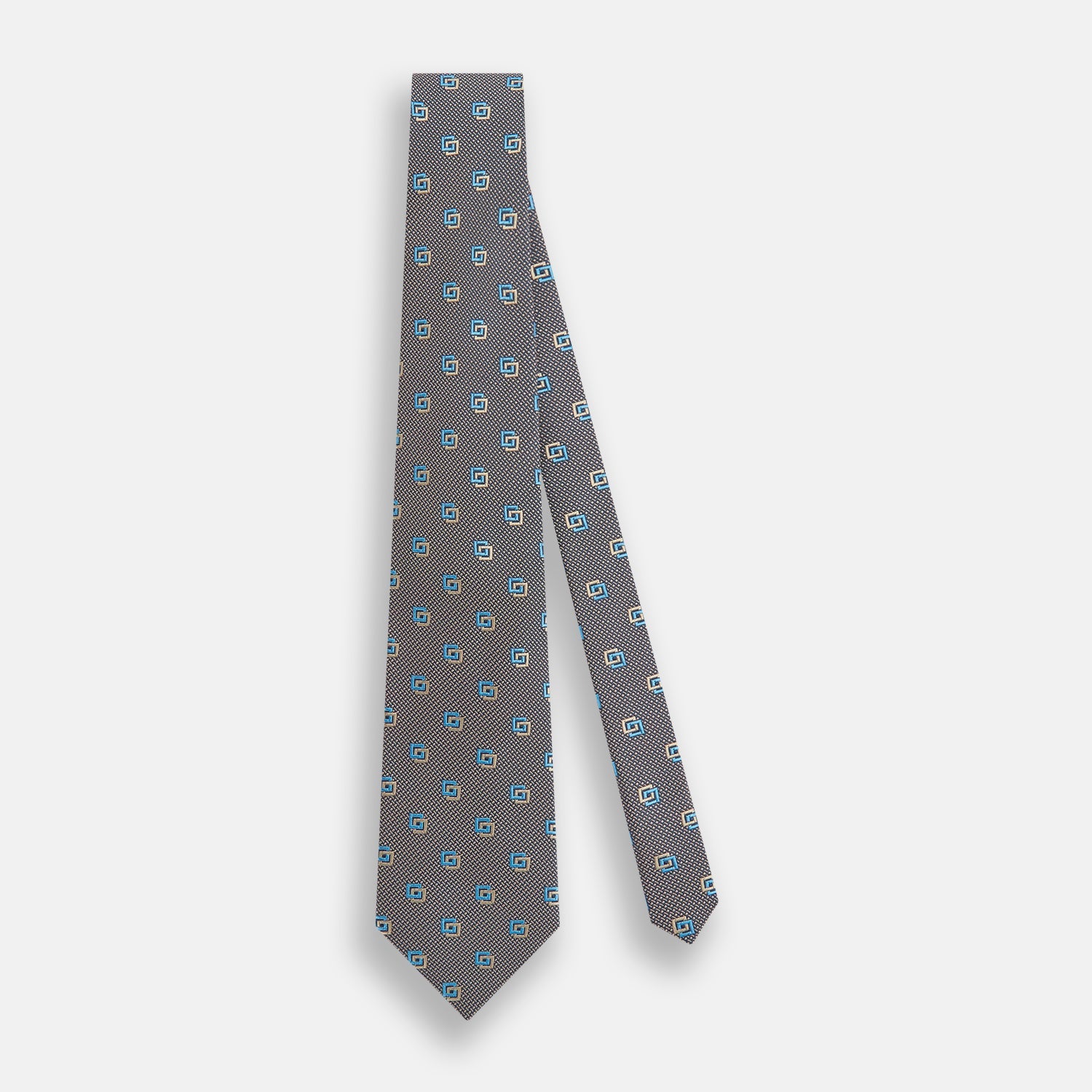 View 2 of product The Turnbull & Asser Blue and Gold Silk Tie, featuring a refined repeating geometric pattern, exudes British elegance and is displayed rolled up on a plain white background.