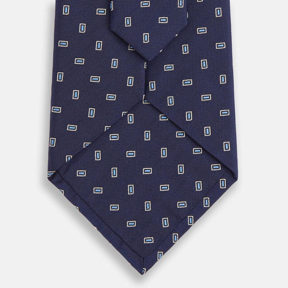 The Turnbull & Asser Navy Micro Rectangle Silk Tie, featuring a repeating light blue and white rectangle pattern, is shown rolled up on a plain white background.