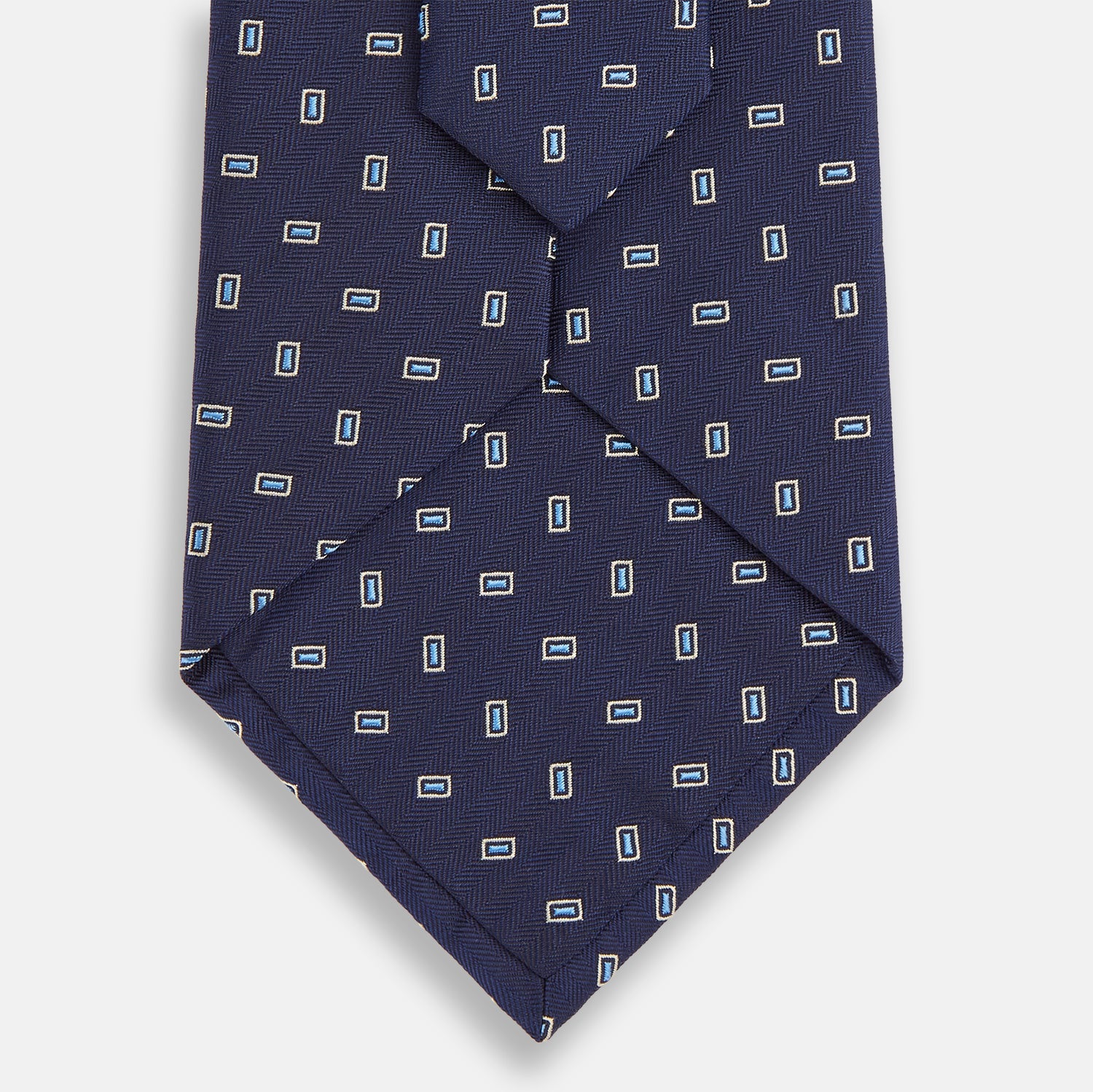 View 3 of product The Turnbull & Asser Navy Micro Rectangle Silk Tie, featuring a repeating light blue and white rectangle pattern, is shown rolled up on a plain white background.
