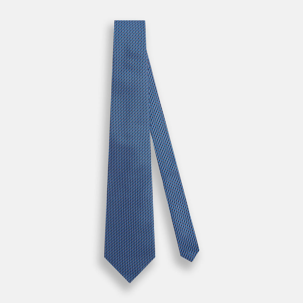 The Turnbull & Asser Blue Geometric Silk Tie features a textured woven pattern with lighter blue accents, shown neatly rolled on a plain white background.