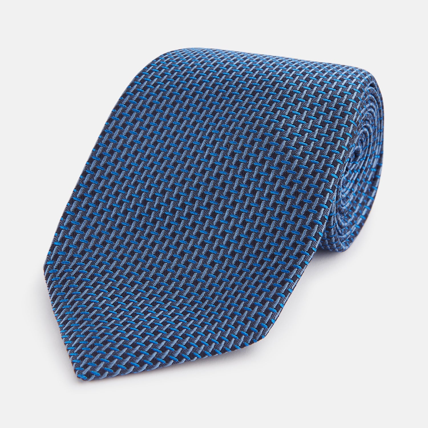 View 1 of product The Turnbull & Asser Blue Geometric Silk Tie features a textured woven pattern with lighter blue accents, shown neatly rolled on a plain white background.