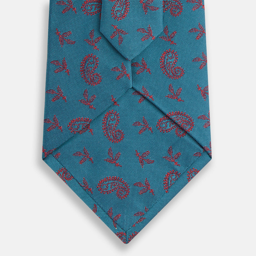 The Teal Paisley Silk Tie by Turnbull & Asser features a red paisley and small floral pattern, shown rolled with the pointed end forward on a white background.