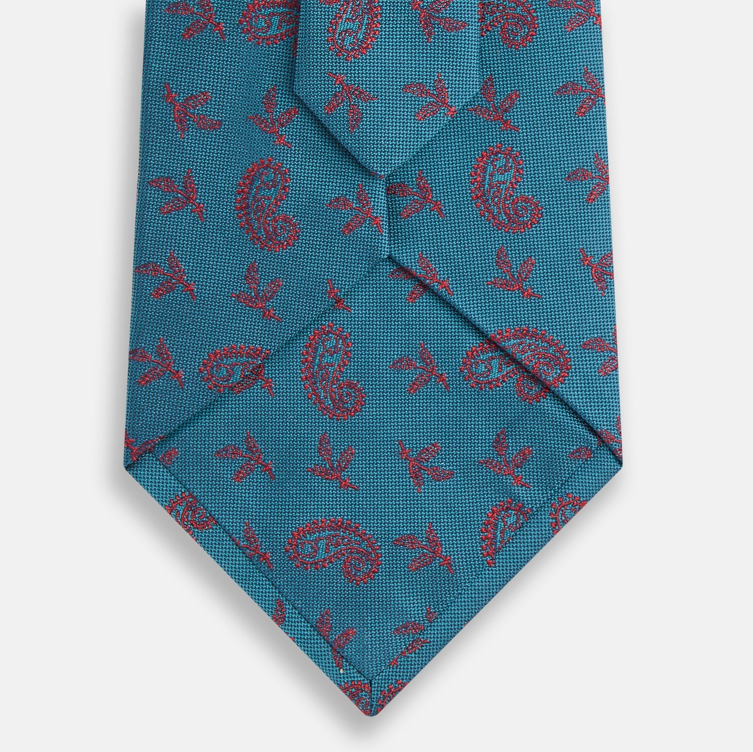 View 3 of product The Teal Paisley Silk Tie by Turnbull & Asser features a red paisley and small floral pattern, shown rolled with the pointed end forward on a white background.