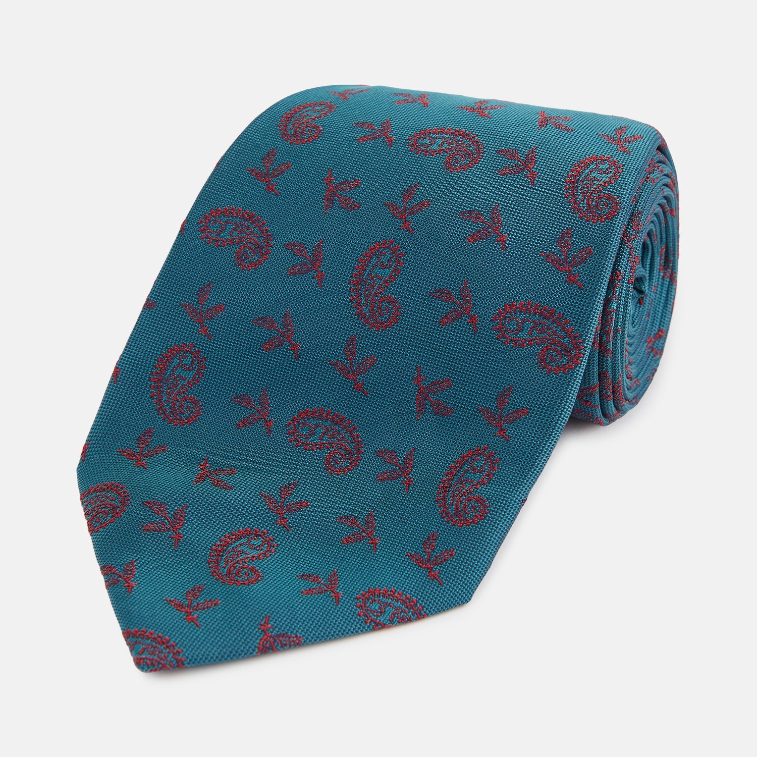 View 1 of product The Teal Paisley Silk Tie by Turnbull & Asser features a red paisley and small floral pattern, shown rolled with the pointed end forward on a white background.