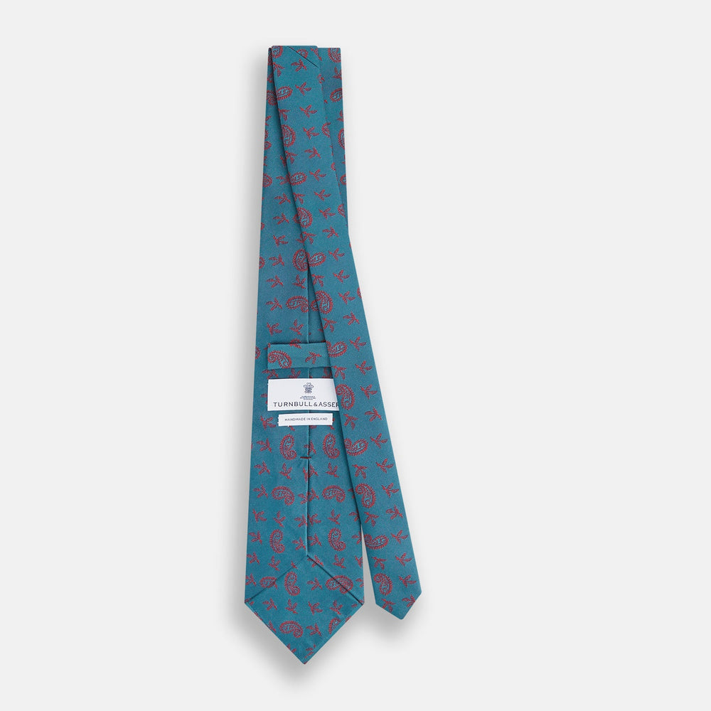 The Teal Paisley Silk Tie by Turnbull & Asser features a red paisley and small floral pattern, shown rolled with the pointed end forward on a white background.