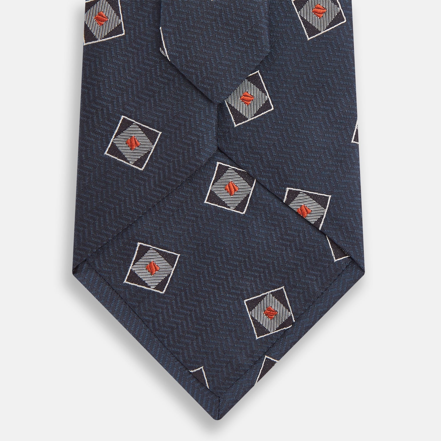 View 3 of product The Turnbull & Asser Grey Square Overlay Silk Tie features a refined chevron pattern with gray square motifs and subtle red accents, expertly handmade for formal occasions. Presented neatly rolled on a white background.