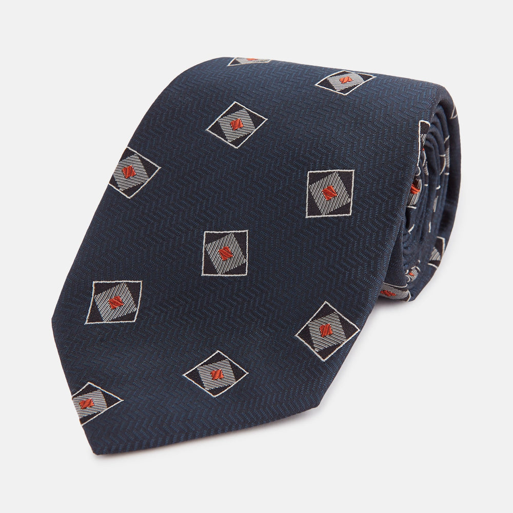 The Turnbull & Asser Grey Square Overlay Silk Tie features a refined chevron pattern with gray square motifs and subtle red accents, expertly handmade for formal occasions. Presented neatly rolled on a white background.
