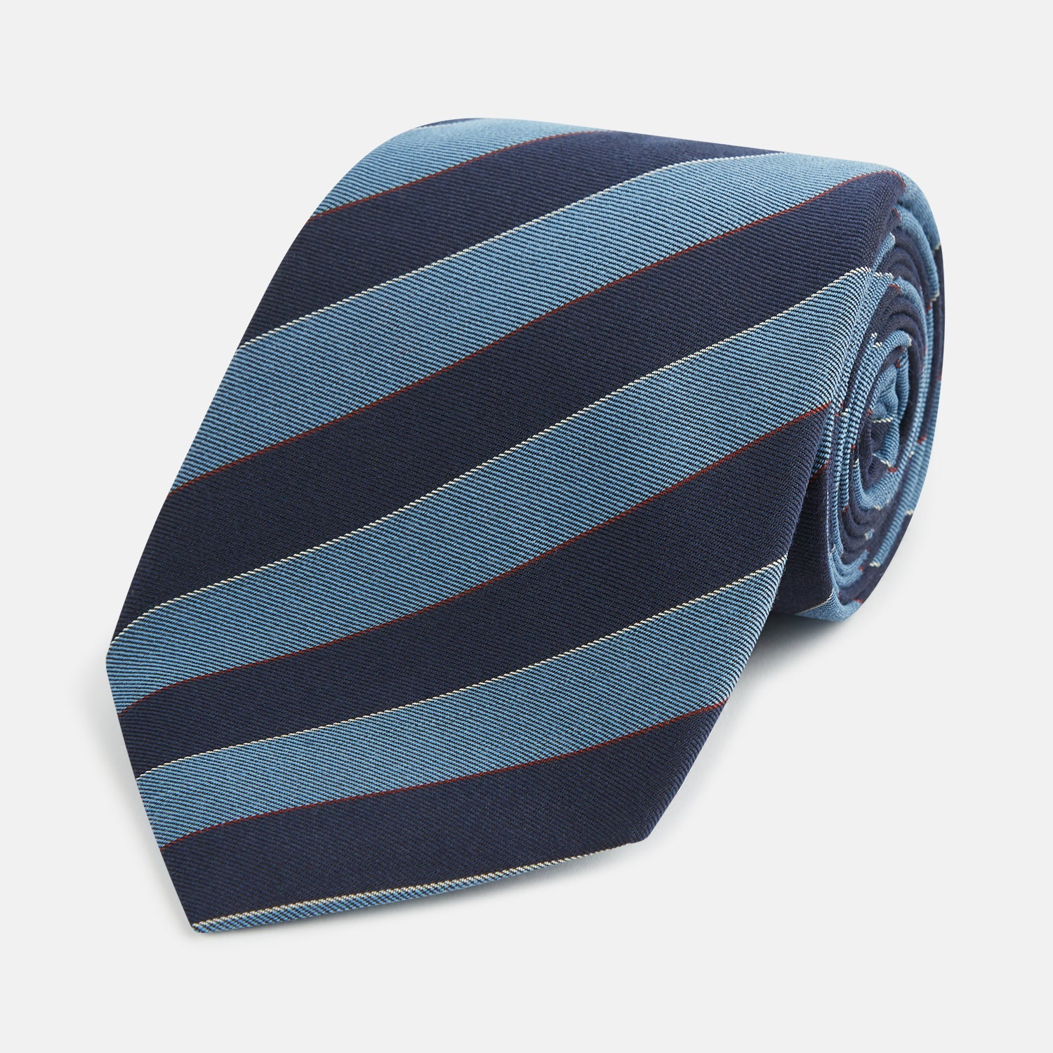 View 1 of product The Blue Block Stripe Silk Blend Tie by Turnbull & Asser features light blue and navy diagonal stripes with thin red lines—a stylish accessory that pairs perfectly with Turnbull & Asser shirts. Displayed rolled-up on a white background.