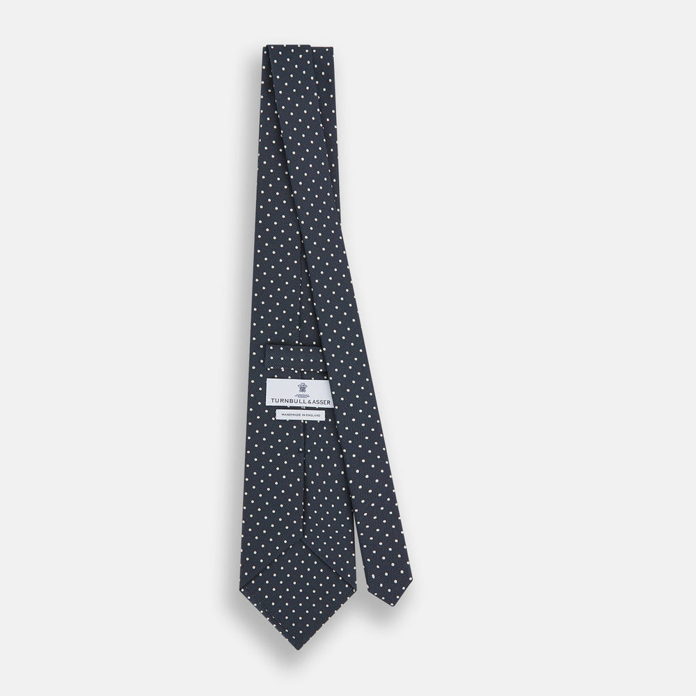 The Turnbull & Asser Navy Micro Dot Silk Tie features a handmade navy blue silk fabric with evenly spaced small white dots, rolled up on a plain white background—a timeless formal accessory for any event.